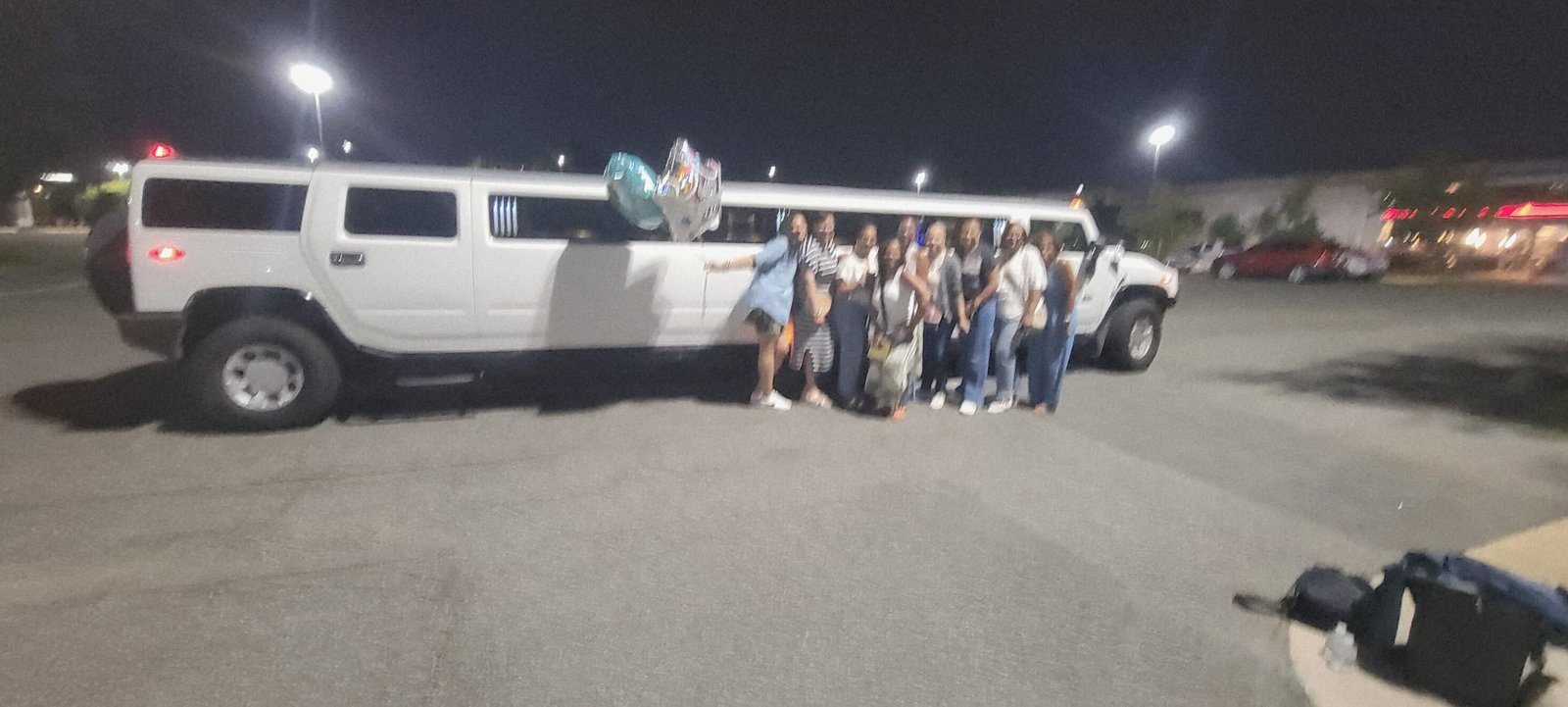 Birthday group posing beside a white Hummer Stretch Limousine at night